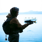 Person holding a fish by a body of water 