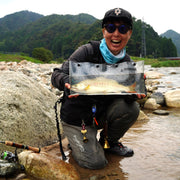 Person holding a clear bag with a fish by a river with mountains in the background