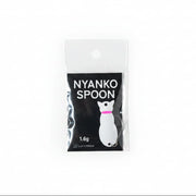 A packaged novelty spoon shaped like a cat, labeled 'NYANKO SPOON' on a black card, placed on a light wood surface.